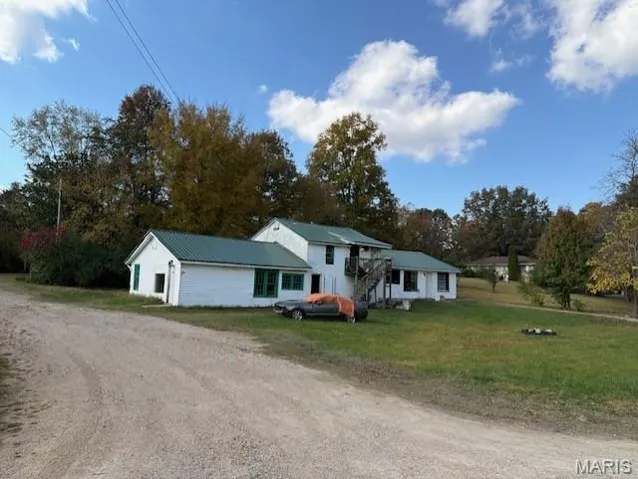 View of front facade featuring stairs, driveway, a front lawn, and view of wooded area