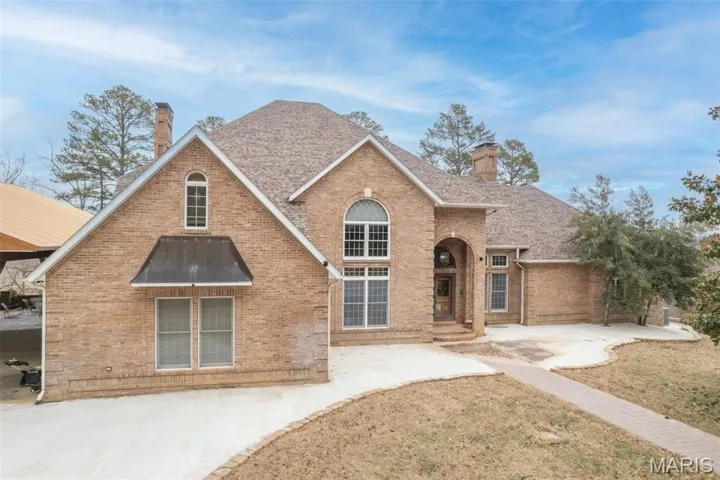 Traditional home featuring a chimney, brick siding, and a shingled roof