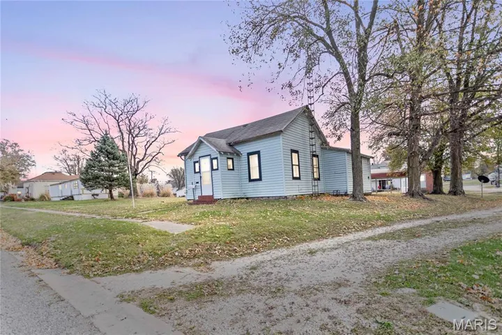 Property exterior at dusk with a lawn and roof with shingles