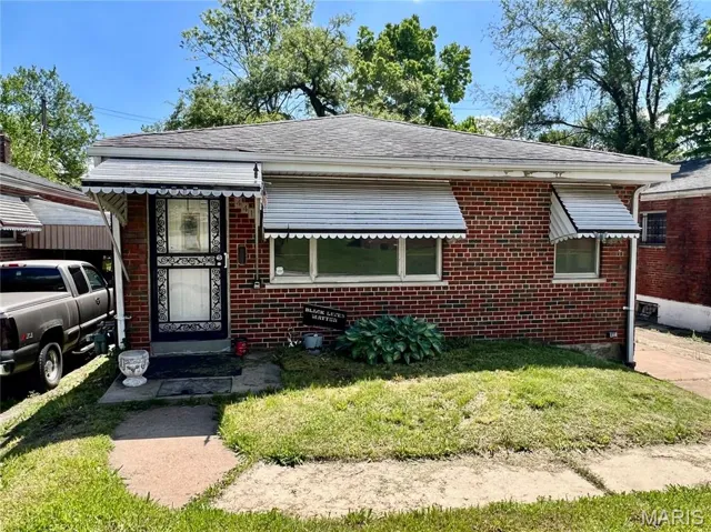 View of front of home with brick siding, a front yard, and roof with shingles