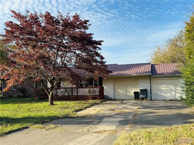 View of front facade with an attached garage, a metal roof, a front yard, and driveway
