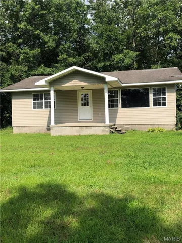 View of front of property featuring covered porch, a front yard, a shingled roof, and view of scattered trees