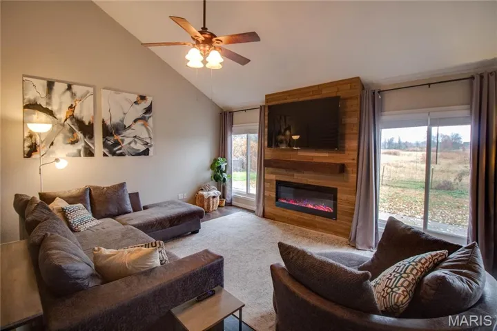 Living room featuring vaulted ceiling, a large fireplace, a ceiling fan, and wood finished floors