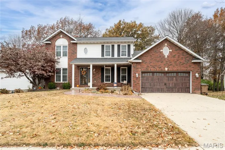 Traditional-style house featuring a porch, concrete driveway, a front yard, and brick siding
