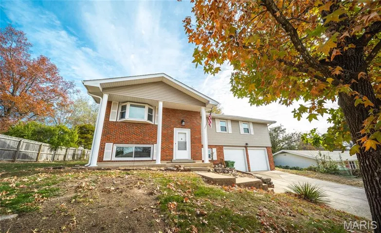 Raised ranch with brick siding, driveway, an attached garage, and covered porch
