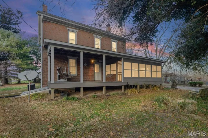 Back of house at dusk with a chimney, brick siding, and a sunroom