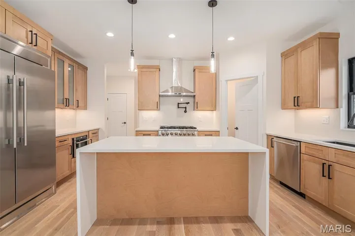 Kitchen with stainless steel appliances, hanging light fixtures, light stone counters, light wood-style floors, and recessed lighting