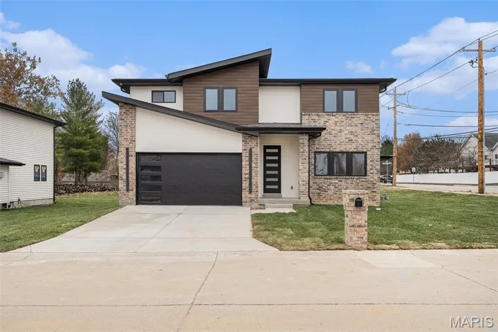 Modern home featuring a front lawn, concrete driveway, brick siding, and an attached garage