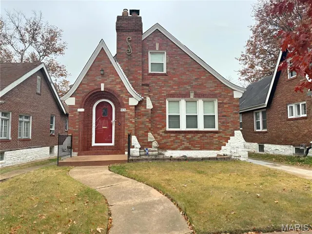 Tudor home with a chimney, a front lawn, and brick siding