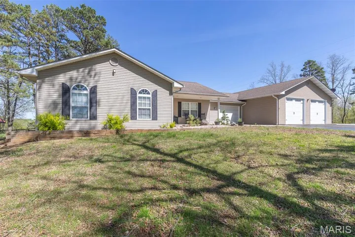 Ranch-style home featuring a front lawn, driveway, a shingled roof, and a garage