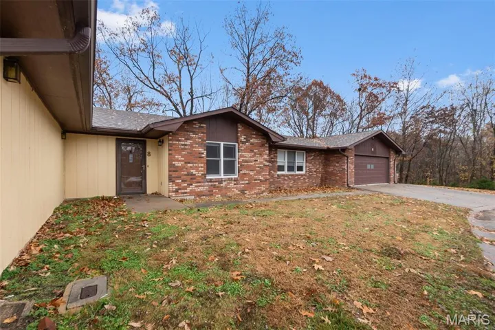 View of front of home with brick siding, driveway, an attached garage, and roof with shingles