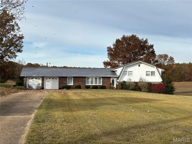 View of front of house with a front lawn, driveway, brick siding, and a metal roof