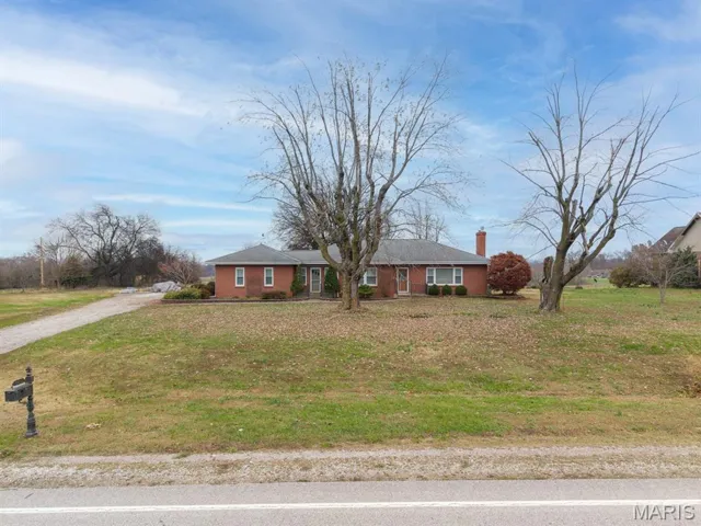 Single story home with brick siding, driveway, a chimney, and a front lawn