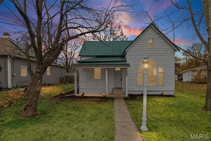 View of front of house featuring a metal roof, covered porch, and a front lawn