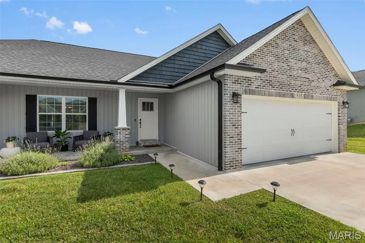 View of front of home featuring a porch, brick siding, an attached garage, driveway, and a front yard