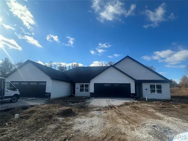Ranch-style home with a garage, brick siding, and dirt driveway