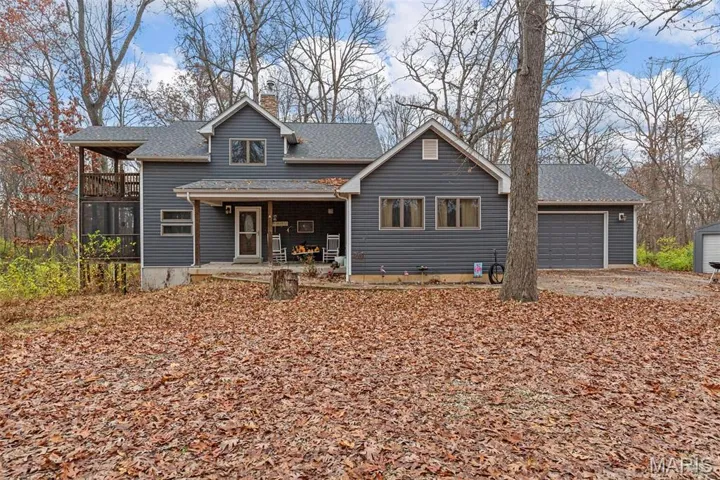 View of front of home with a chimney, a shingled roof, an attached garage, and a patio area