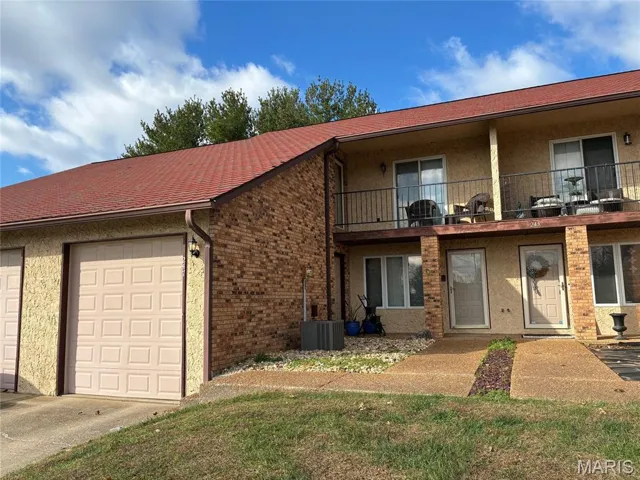 View of front of property featuring a balcony, stucco siding, and brick siding