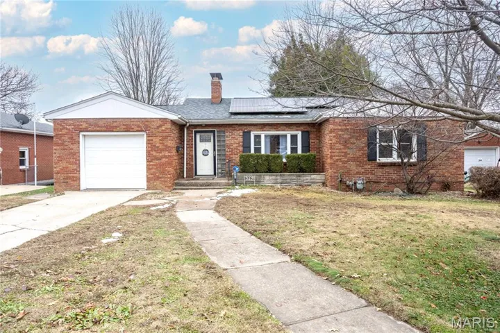 Ranch-style home featuring a front yard, roof mounted solar panels, brick siding, a chimney, and a garage