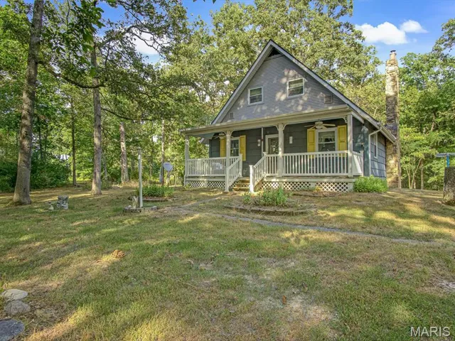 View of front of home with a porch, a chimney, a front lawn, ceiling fan, and view of scattered trees