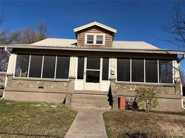 View of front of property with a sunroom, a metal roof, and a front yard