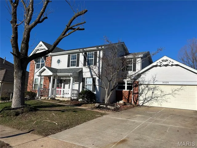 View of front of house with brick siding, covered porch, a front lawn, driveway, and a garage