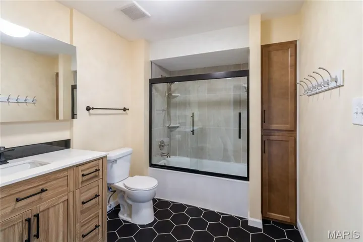 Full bathroom with bath / shower combo with glass door, vanity, and dark tile patterned flooring