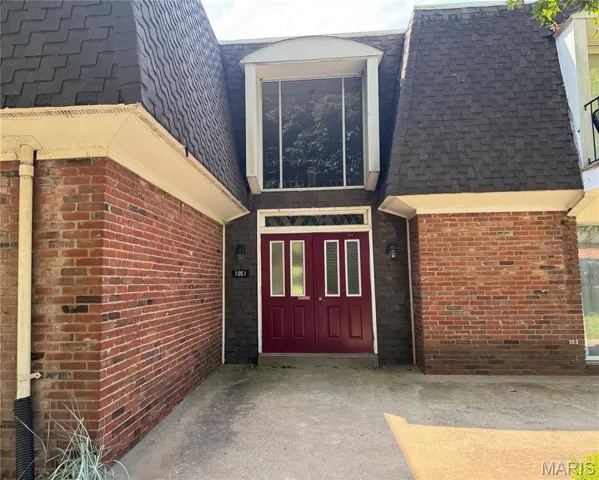 Entrance to property with a shingled roof, brick siding, and mansard roof