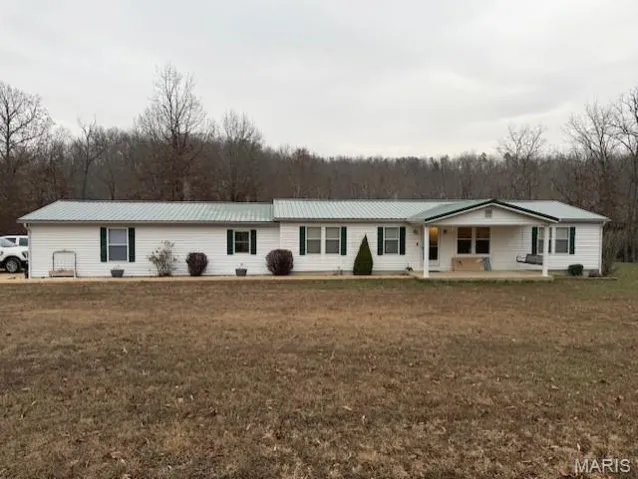 Ranch-style house featuring a metal roof, a porch, a wooded view, and a front lawn