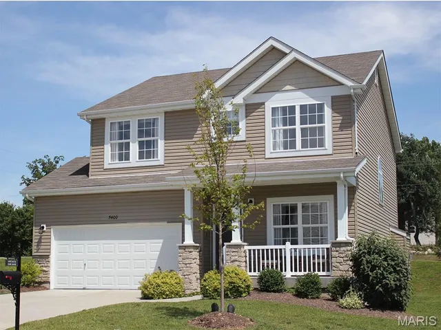 View of front of property with stone siding, a shingled roof, a porch, a garage, and a front yard