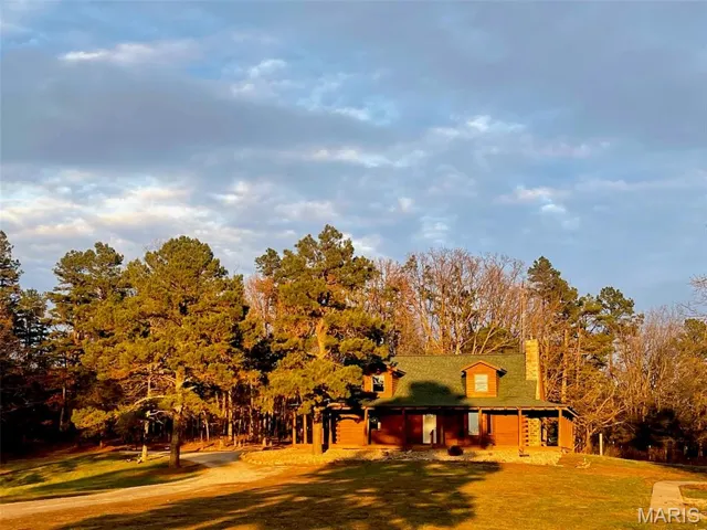 View of front of house featuring covered porch, a chimney, view of wooded area, and a front lawn