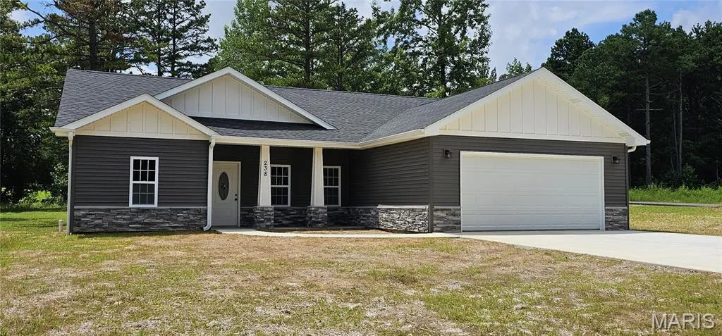 View of front of home with stone siding, board and batten siding, a shingled roof, and an attached garage