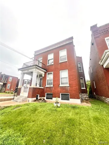 Rear view of property with a yard, a balcony, brick siding, and a patio