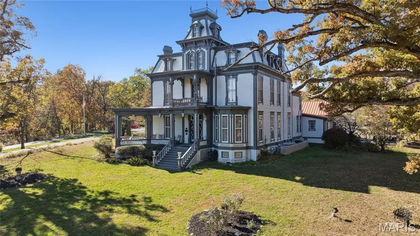 View of front of property featuring a chimney, a front lawn, a porch, and mansard roof