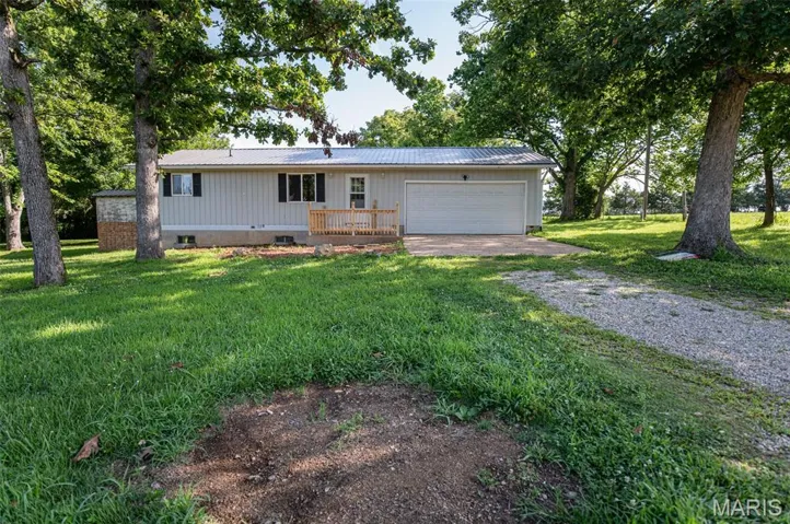 Ranch-style house featuring driveway, a metal roof, an attached garage, a front lawn, and board and batten siding