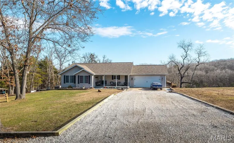 Single story home with covered porch, gravel driveway, a shingled roof, a front yard, and an attached garage