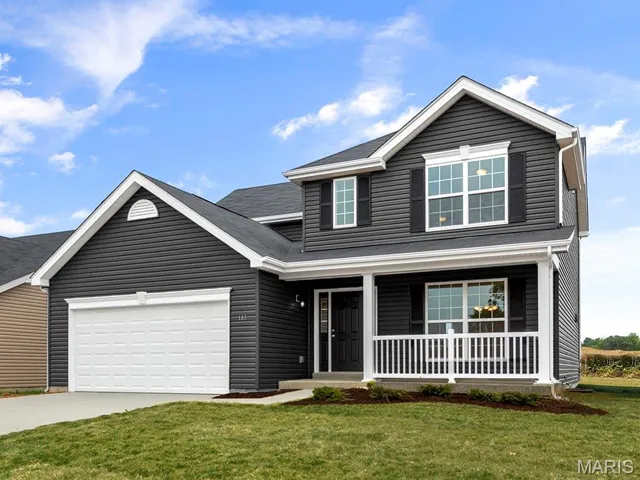Traditional-style house with a front lawn, covered porch, concrete driveway, and an attached garage
