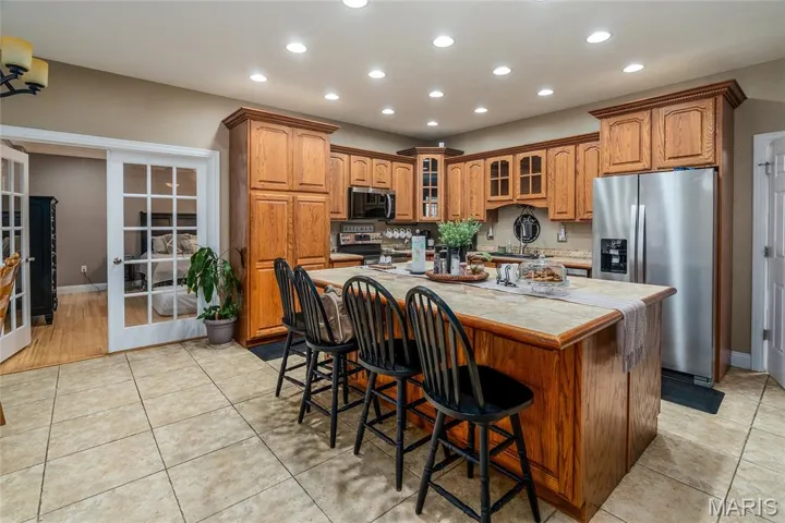 Kitchen featuring brown cabinetry, a center island, glass insert cabinets, a breakfast bar area, and stainless steel appliances
