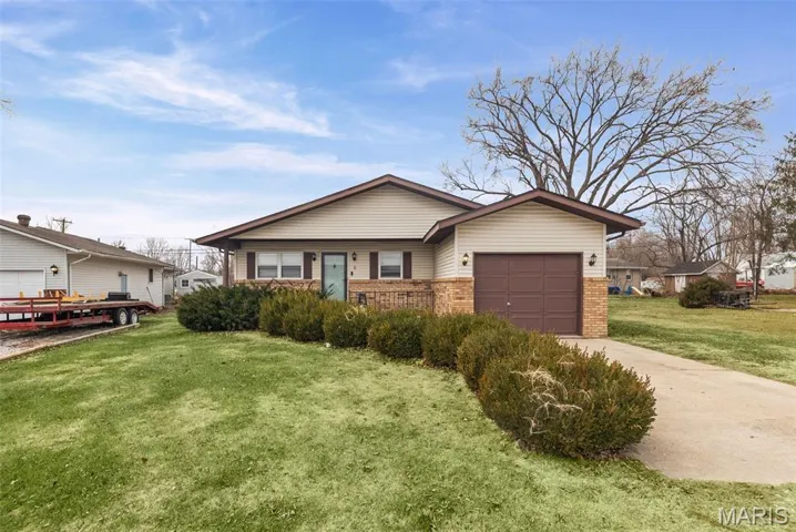 View of front of home with brick siding, an attached garage, a front lawn, and driveway