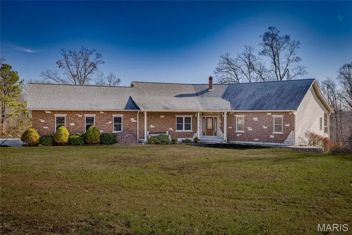 View of front of house with a front yard, a porch, a shingled roof, and brick siding