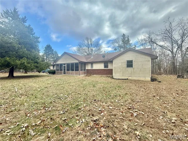 Back of property with a sunroom and a lawn