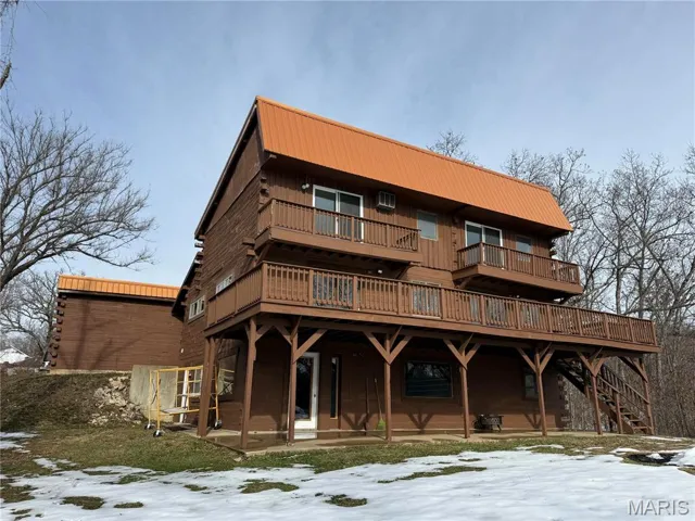 View of front facade with a wooden deck, a metal roof, a balcony, and a patio