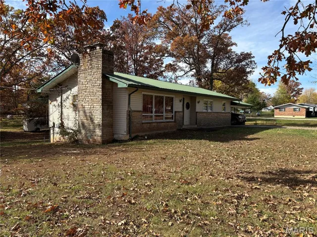 View of front of property with a chimney, a front lawn, brick siding, and a metal roof