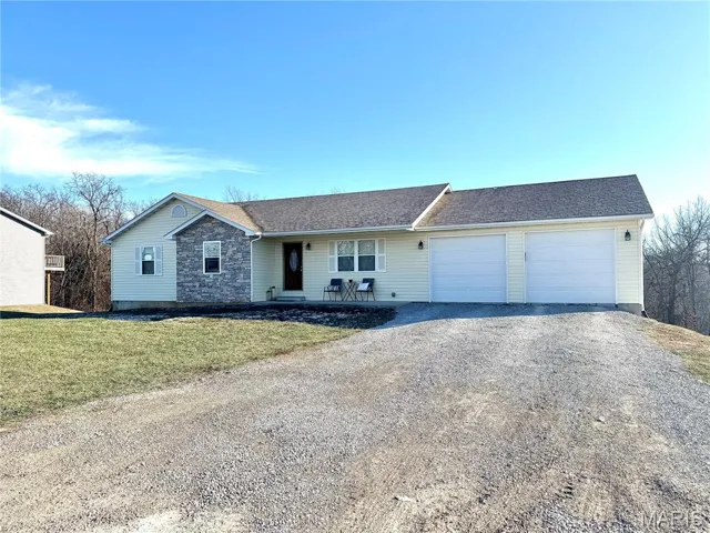 Ranch-style house with gravel driveway, a shingled roof, a garage, a front lawn, and stone siding