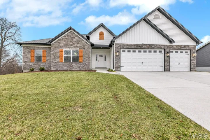 View of front of home featuring driveway, a front yard, an attached garage, board and batten siding, and stone siding