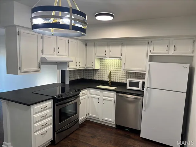 Kitchen featuring appliances with stainless steel finishes, white cabinetry, dark countertops, and dark wood-type flooring