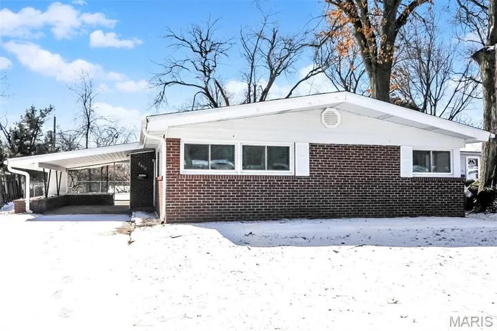 View of snow covered exterior featuring brick siding and an attached carport