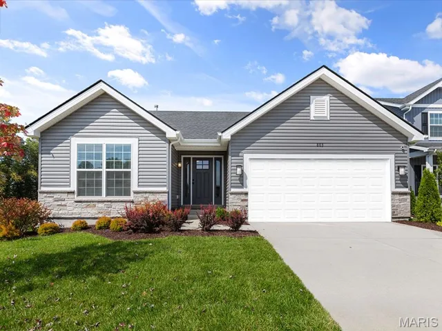 View of front facade with stone siding, a front yard, driveway, a garage, and roof with shingles