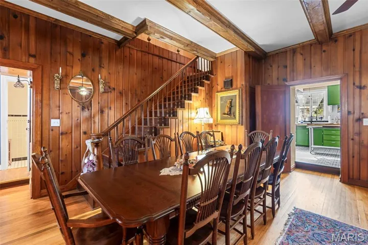 Dining room with stairway, beamed ceiling, light wood finished floors, and wood walls