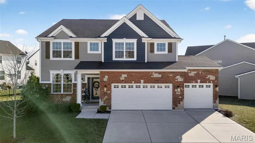 View of front facade featuring brick siding, a front lawn, concrete driveway, roof with shingles, and a garage